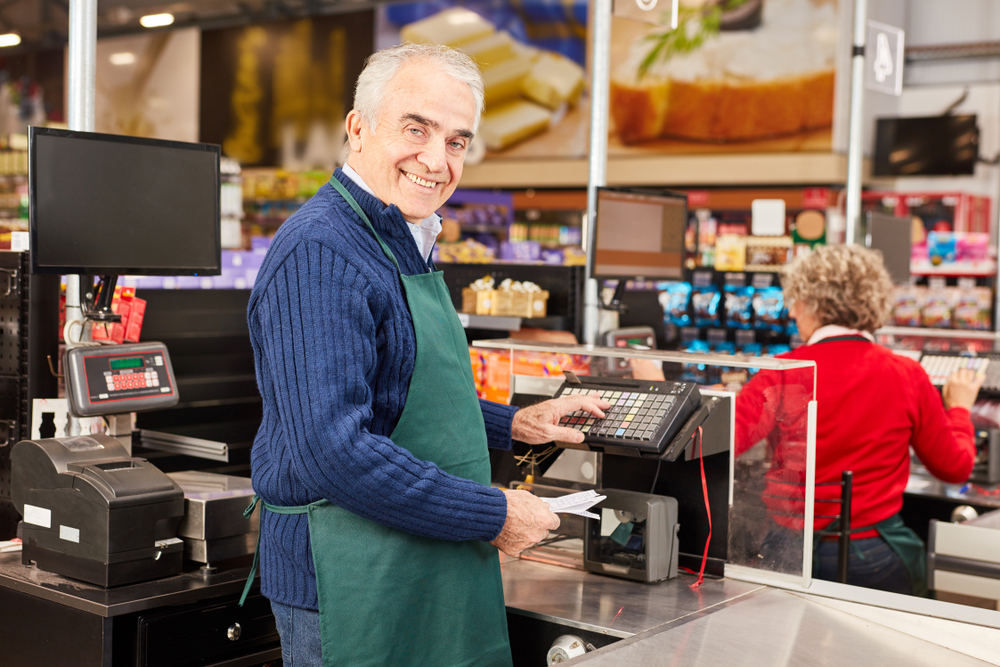 homem idoso usando um avental e sorrindo em um caixa de supermercado