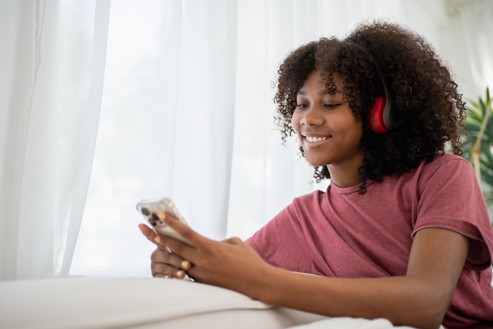 Mulher jovem empreendedora com fones de ouvido sorri enquanto olha para o celular