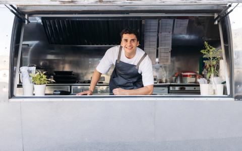 Homem jovem empreendedor de avental sorri dentro de um food truck